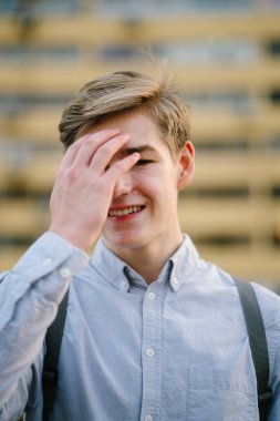 Ayakta ve gülümseyen bir genç çekici beyaz erkek samimi portresi. O arka planda bina bir sarı ile şehirde ve raslantı henüz akıllıca giyindi.