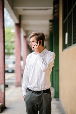 Stüdyo portre gülümseyen genç bir beyaz adam. İş smartphone ile rahat giyiniyor. O genç, yakışıklı, fotojenik ve mutlu, kendine güvenen ve heyecanlı görünüyor.