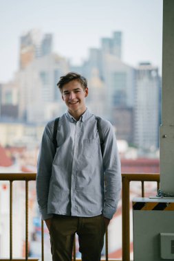 Ayakta ve gülümseyen bir genç çekici beyaz erkek samimi portresi. O arka planda bina bir sarı ile şehirde ve raslantı henüz akıllıca giyindi.