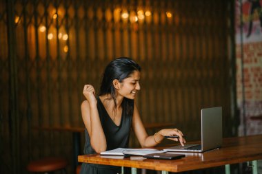 Onun laptop rahat bir kafede çalışan ya da uzay coworking çekici ve genç Hint (Asya) profesyonel samimi portresi. O bir dizüstü ve tablet yakın vardır. Onu laptop gülümsüyor.