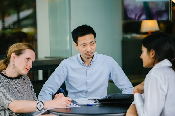 young Indian Asian woman is interviewing for a job and is speaking with a diverse interview panel in an office in the day. One interviewer is a Chinese man and the other a caucasian woman.