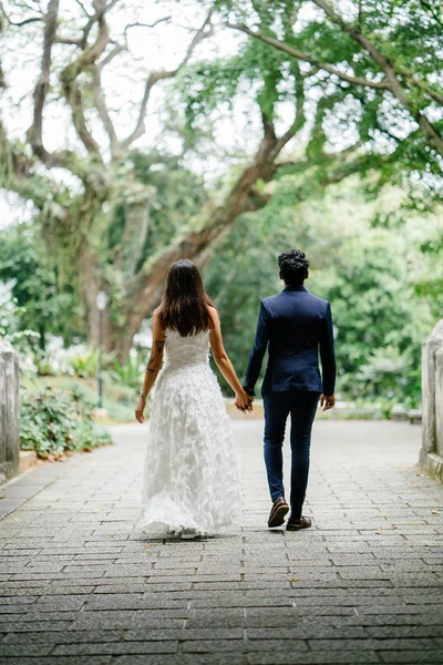 Interracial Asian couple walking in the park. An Indian man is engaged to a Chinese moment and they are taking wedding photographs in a beautiful park in the day.