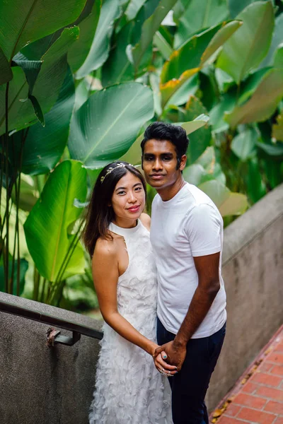 Portrait of young, interracial couple taking photos after getting engaged in Fort Canning, Singapore. They are laughing and playing around; happy and excited about their future.