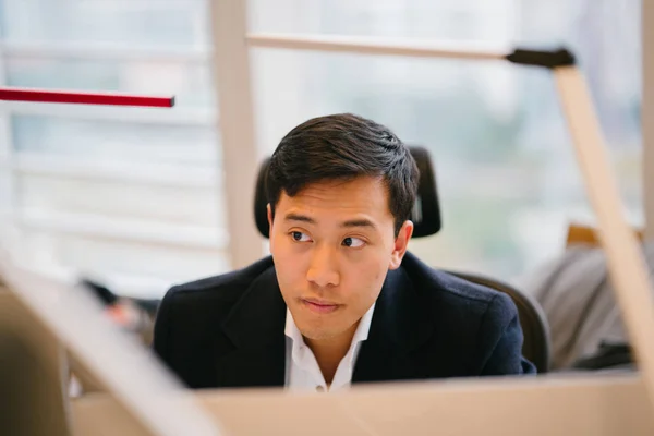 young Chinese Asian trader and banker in finance looks at his screen in intense concentration. He is dressed in a professional suit and in an office.