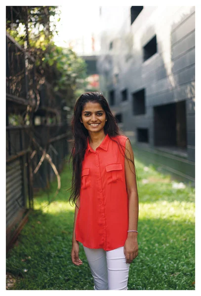 Portrait of a young Indian student or business person smiling with a campus, university or coworking space in the background. She\'s wearing an orange blouse