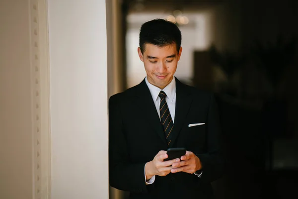 Portrait of young and handsome Chinese Asian man in a suit with his smartphone.