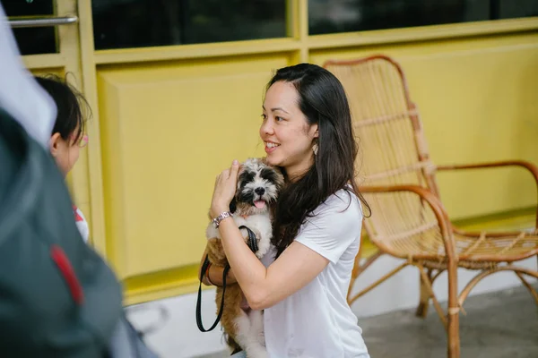 Portrait of a young Pan Asian woman with dog  on a warm day in the park. The dog is a toy breed shih tzuh.