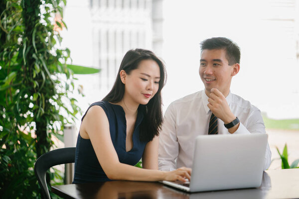 Portrait of two smiling business people (lawyers, consultants, etc) or couple smiling mid discussion over a laptop in an office with greenery in the background. They are focused on the laptop.
