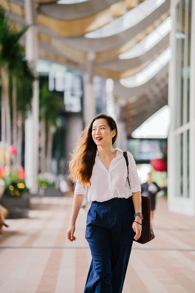 Portrait of a young Singaporean Chinese Asian woman executive walking outdoors in the city. She is smartly and elegantly dressed in corporate wear and is walking.