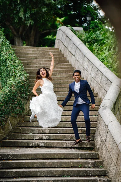 young interracial couple (Indian man, Chinese woman) take wedding photos in Fort Canning Park, Singapore.
