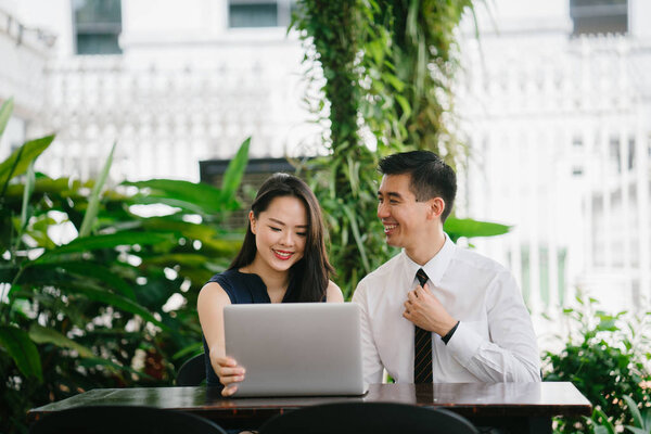 Portrait of two smiling business people (lawyers, consultants, etc) or couple smiling mid discussion over a laptop in an office with greenery in the background. They are focused on the laptop.