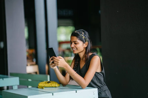 Candid portrait of an attractive and young Indian Asian professional woman reading her tablet or e reader. She is in warm, cosy cafe or coworking space. She is smiling while she reads her tablet.