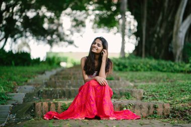 Günde bir parkta oturan çekici, genç Hint (Asya) kadın portresi adımlar.