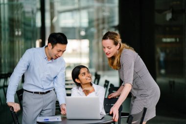 farklı bir takım 3 kişi bir dizüstü bilgisayar etrafında bir tartışma gün açık bir alanda yaşıyorsanız. Gülümse ve konuşmak gibi enerjik ve neşeli vardır.