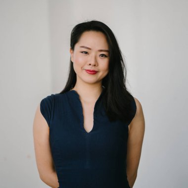 Düz beyaz arka plan karşı genç bir Asyalı kadın portre kafa vurdu. O Lacivert bir elbise giyiyor ve şık ve zarif giyindi ve Görüntüleyici gülümsüyor.