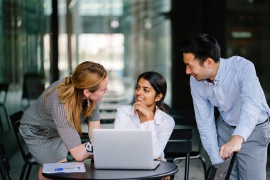 farklı bir takım 3 kişi bir dizüstü bilgisayar etrafında bir tartışma gün açık bir alanda yaşıyorsanız. Gülümse ve konuşmak gibi enerjik ve neşeli vardır.