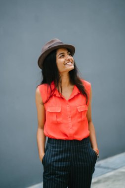 Bir genç, çekici Hint Asya portresi öğrenci moda. O gülümseyen ve güneşin düz gri mavi arka plan karşı ayakta.