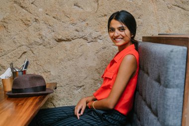 Kameraya gülümseyen bir genç ve çekici Hint Asyalı kadın portresi. O oturduğundan ve bir kahverengi fedora kap vardır. O akıllı rahat giyinmiş ve rahat ve neşeli.