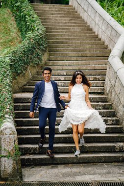 Interracial aşıklar çifti parkta taş merdivenlerden gün boyunca çalıştırın. Bir Hintli Çinli bir kadını evleniyor ve onlar zevk ve neşe içinde merdivenlerden aşağı çalışan.