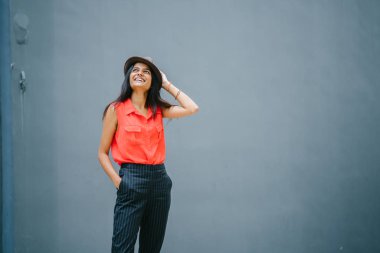 Bir genç, çekici Hint Asya portresi öğrenci moda. O gülümseyen ve güneşin düz gri mavi arka plan karşı ayakta.