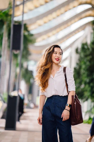 A young and stylish Chinese businesswoman in the city in Singapore. She is Chinese (Singaporean) and is dressed professionally and elegantly. She is relaxed and smiling at the camera.