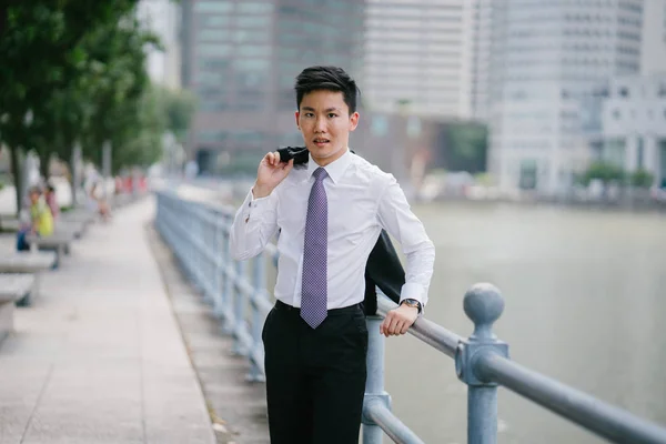 Portrait of Asian man  along the Singapore River in the day. He's professionally dressed in a white shirt, tie