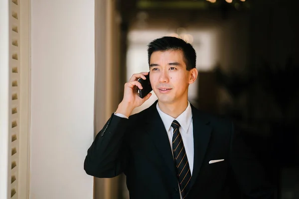 Portrait of young and handsome Chinese Asian man in a suit with his smartphone.