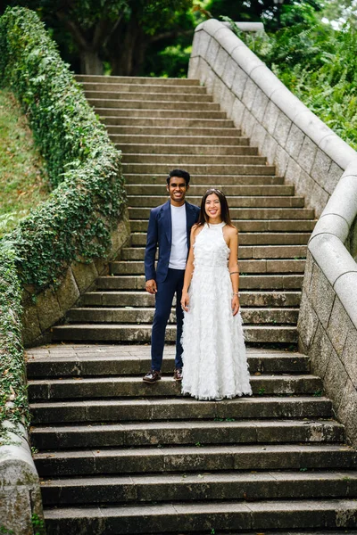pair of interracial lovers on stone steps in the park during the day. An Indian man is marrying a Chinese woman  in delight and joy.