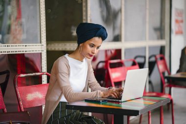 Bir genç, çekici Müslüman kadın (Asya, Arap, Malay) girişimci veya onu laptop çalışma işkadını portresi. O akıllıca giyindi ve (türban, başörtüsü) sarık takıyor ve oturuyor.