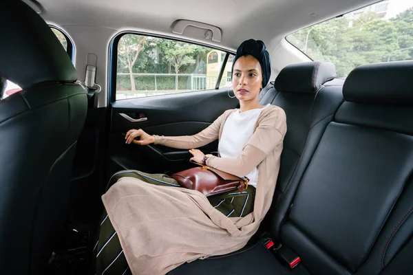 Portrait of a young, attractive Muslim woman  in a private limousine. She is wearing a turban and smartly but modestly dressed in the backseat