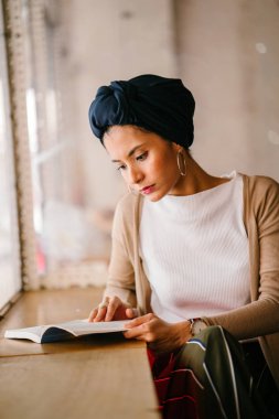 genç, çekici Müslüman kadın (Arap, Malay, Asya) günde bir kafe pencere tarafından bir kitap okur. O bir Türban (başörtüsü, hijabi) giyiyor ve dünyevi tonlarda zarif giyinmiş.