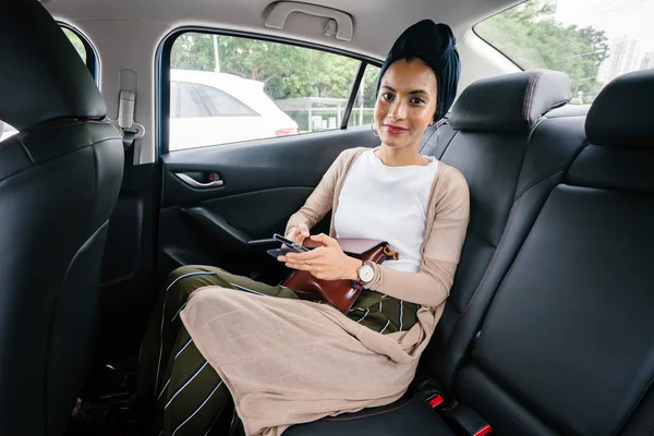 専用リムジンで電話で若い 魅力的なイスラム教徒の女性の肖像画 彼女はターバンを身に着けているとスマートが控えめな後部座席で服を着て 彼女のスマート フォンの話 — ストック写真