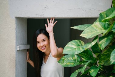 Duvarları olan bir bitki karşı bir coworking alanda profesyonel bir ince, genç ve çekici Çinli kadın portresi. O gülümseyen ve profesyonel olarak beyaz bir elbise giymiş..