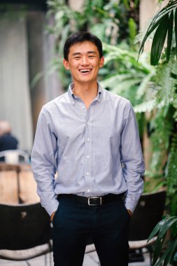 Yakışıklı, genç, akıllı portresi Çinli Asyalı adam gülümseyerek ve gün yeşil bir duvara karşı duran bir takım. Kısa saçlı ve gri takım elbise giyiyor.