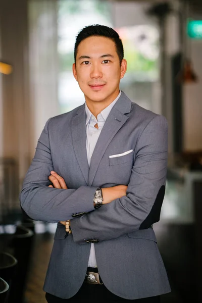 Portrait of a young, professional and handsome Chinese Asian lawyer. He is in a grey suit and white pocket square and is smiling at the camera. He is well groomed and put together and is smiling.