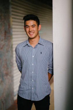 Yakışıklı, genç, akıllı portresi Çinli Asyalı adam gülümseyerek ve gün duvara karşı duran bir takım. Kısa saçlı ve gri takım elbise giyiyor.