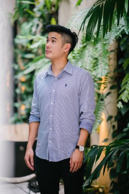 Yakışıklı, genç, akıllı portresi Çinli Asyalı adam gülümseyerek ve gün yeşil bir duvara karşı duran bir takım. Kısa saçlı ve gri takım elbise giyiyor.