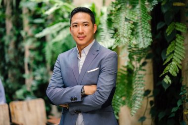 Yakışıklı, genç, akıllı portresi Çinli Asyalı adam gülümseyerek ve gün yeşil bir duvara karşı duran bir takım. Kısa saçlı ve gri takım elbise giyiyor.