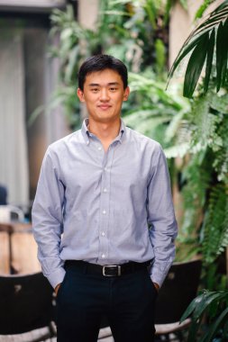 Yakışıklı, genç, akıllı portresi Çinli Asyalı adam gülümseyerek ve gün yeşil bir duvara karşı duran bir takım. Kısa saçlı ve gri takım elbise giyiyor.