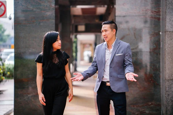 stock image portrait of two professional business people walking and talking. They are deep in conversation as they walk on a street in a city in Asia. The man and woman are both professionally dressed.