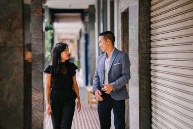 yürüyen ve konuşan iki profesyonel iş adamları portresi. Asya'da bir şehirde bir sokakta yürürken derin konuşmada değilsiniz. Her ikisi de profesyonel olan erkek ve kadın giyinmiş.