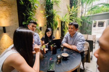 Grup Asya iş bir masa etrafında oturup çalışmaları hakkında sohbet vardır. Onlar konuşurken onlar gülümseyen ve rahat.