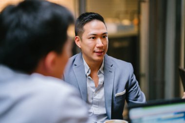 Grup genç ve enerjik Çin iş arkadaşlarınızla bir masa etrafında oturup bir ışık var Asya iş tartışma yürekli. Gülümseyen ve onlar konuşmak ve sohbet gibi gülüyor.