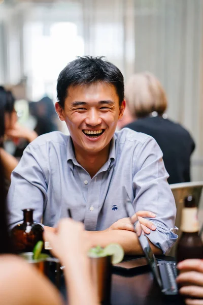 group of young and energetic Chinese Asian coworkers sit around a table and have a light hearted business discussion. They are smiling and laughing as they talk and have a conversation.