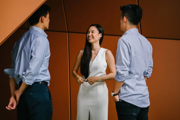 team of three business professionals (lawyers, bankers or accountants) have a conversation / discussion in their office in the day. Two Chinese Asian men and a woman stand together and are talking.
