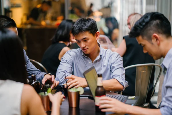 group of young and energetic Chinese Asian coworkers sit around a table and have a light hearted business discussion. They are smiling and laughing as they talk and have a conversation.