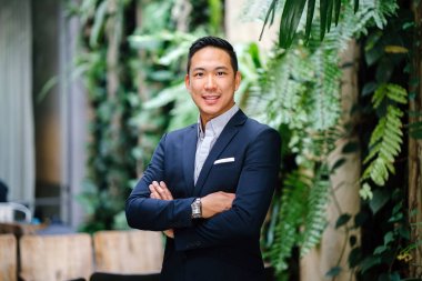 Yakışıklı, genç, akıllı portresi Çinli Asyalı adam gülümseyerek ve gün yeşil bir duvara karşı duran bir takım. Kısa saçlı ve gri takım elbise giyiyor.