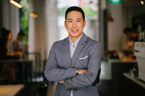 Portrait of a young, professional and handsome Chinese Asian lawyer. He is in a grey suit and white pocket square and is smiling at the camera. He is well groomed and put together and is smiling.