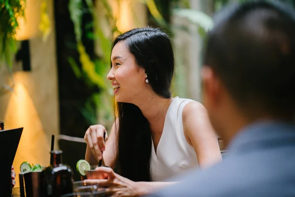 young Chinese woman professional (lawyer, banker, lawyer, etc) smiles and laughs as she has a discussion with coworker in a trendy coworking space or office over drinks. She is young and attractive
