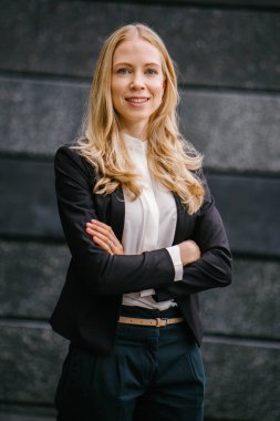 Bir beyaz, portre profesyonel bir takım bir koyu gri arka plan beyaz ve çekici orta yaşlı bir kadın. Sarı saçları ve mavi gözleri ve gülümseyen güzel bir kız 